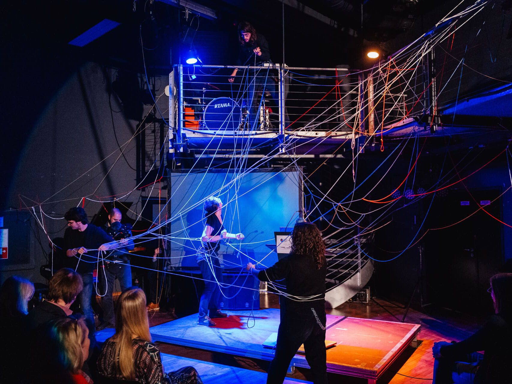 Theaterbühne mit Schauspieler:innen, die Fäden verwirren